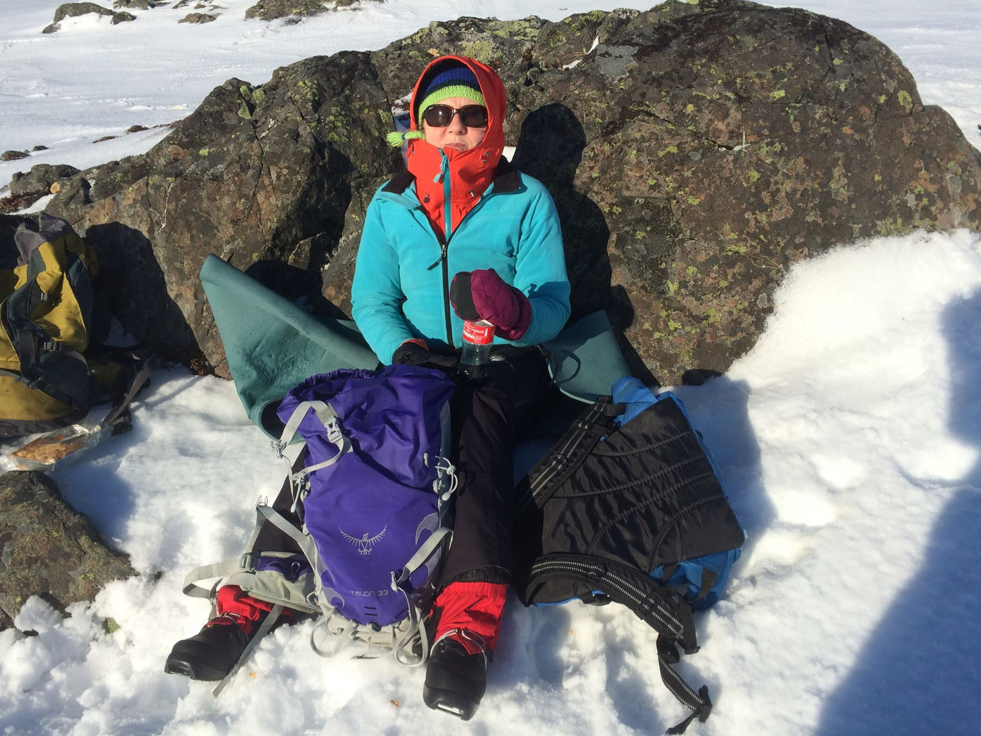 Helen i vinterklær lent mot en stein på Breitind med snø rundt seg