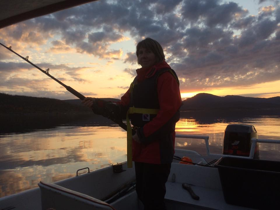 Helen i redningsvest med fiskestang i båten under en gyllen solnedgang