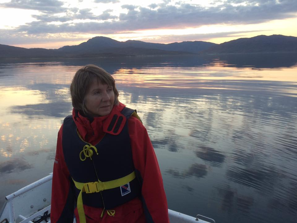 Helen i båten med speilblankt vann og fjell i bakgrunnen i kveldslys