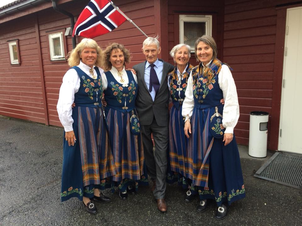 Helen og søstrene i bunad sammen med en herre foran et rødt hus med norsk flagg