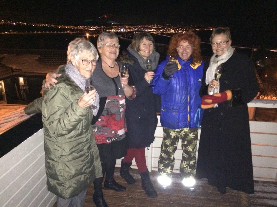Helen og venninner skåler med champagne på terrassen med byen i bakgrunnen